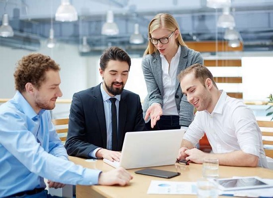 IT consultants and business professionals collaborating on a project with a laptop in a modern office setting, discussing digital transformation and strategy.