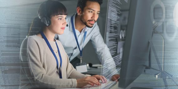 Two cybersecurity professionals analyzing real-time data on a high-tech screen in a secure operations center, wearing headsets and ID badges.