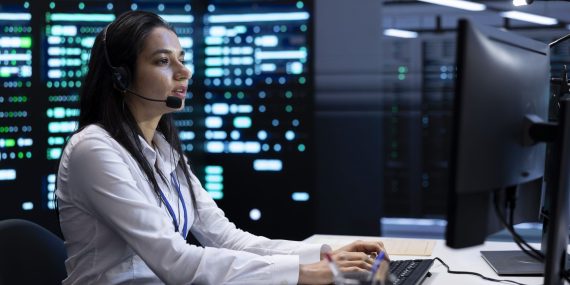 IT support specialist working in a data center with headset, monitoring servers and providing technical assistance.